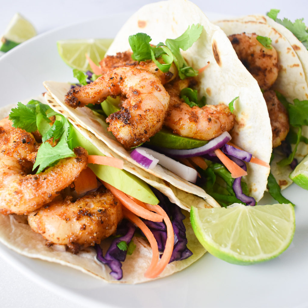 2 prawn tacos on a plate with 2 in the background.