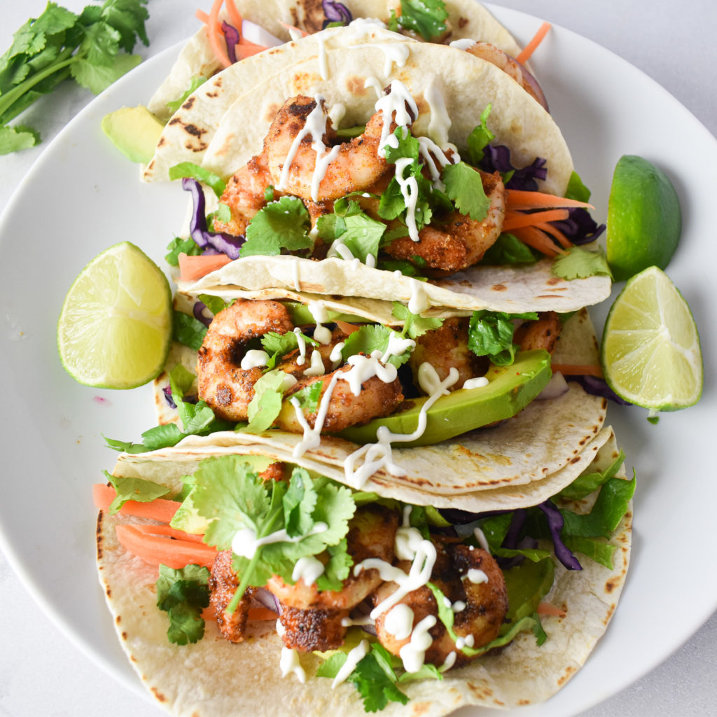 4 prawn tacos on a plate with sour cream dressing.