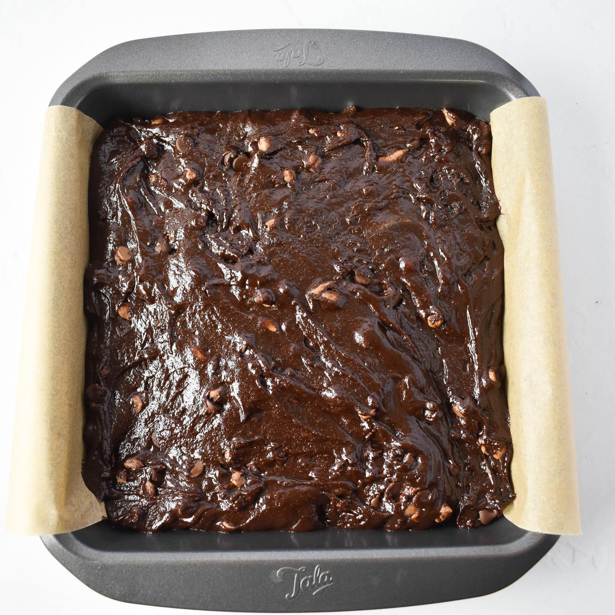 Brownie batter in lined baking tin.