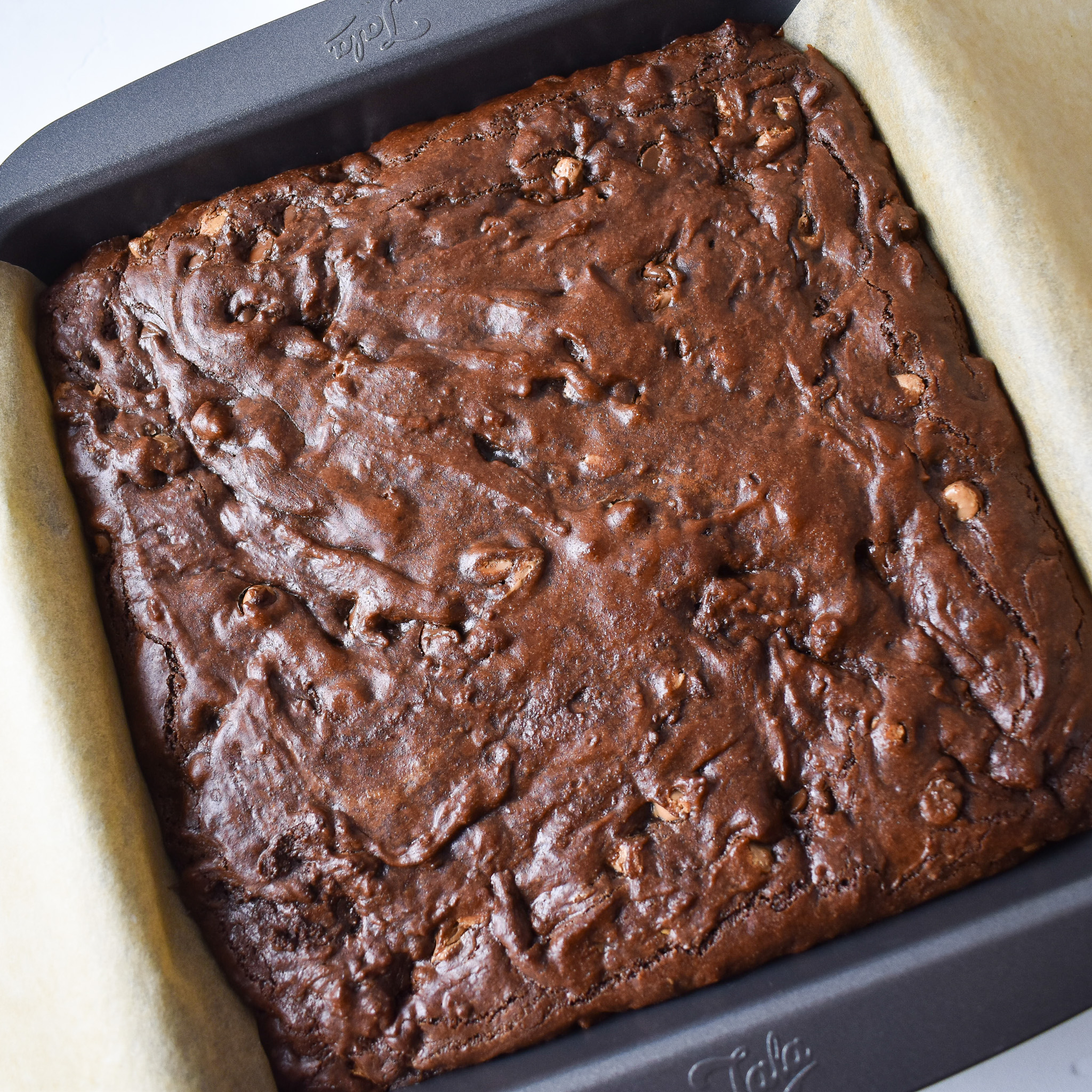 Whole uncut baked brownie in baking tin.