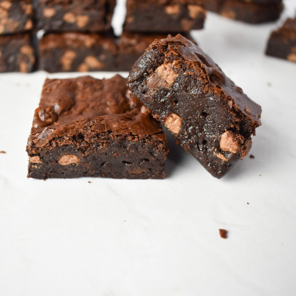 2 Fudgy Brownies squares with brownies in background.