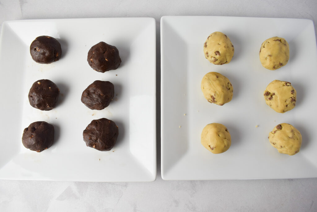 Unbaked cookie dough balls. There are 2 plates: 1 with double chocolate cookie dough balls and 1 plate with regular cookie dough balls.