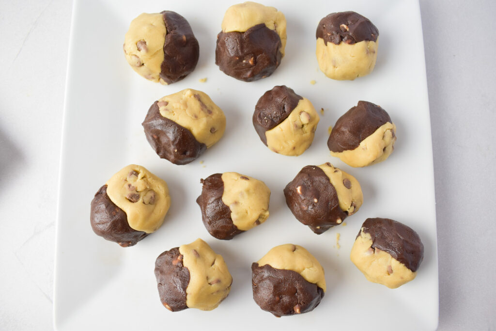 Unbaked cookie dough balls on a plate. Half double chocolate and half regular cookies dough.