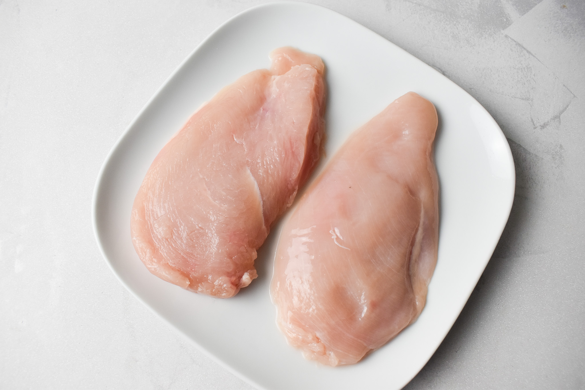 Raw chicken breast sliced in half lengthway on small [plate.