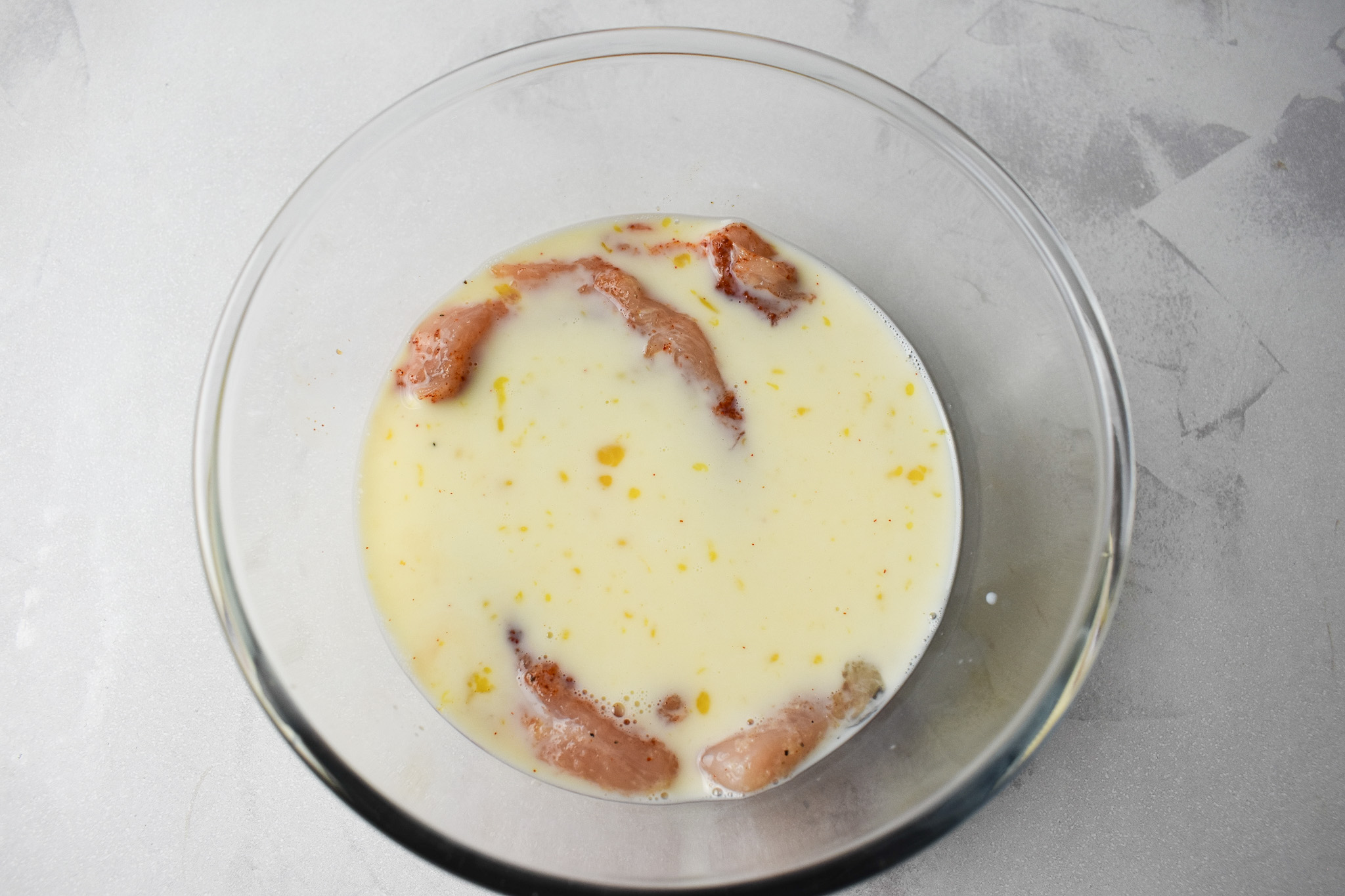 Chicken soaked in buttermilk mixture in clear bowl