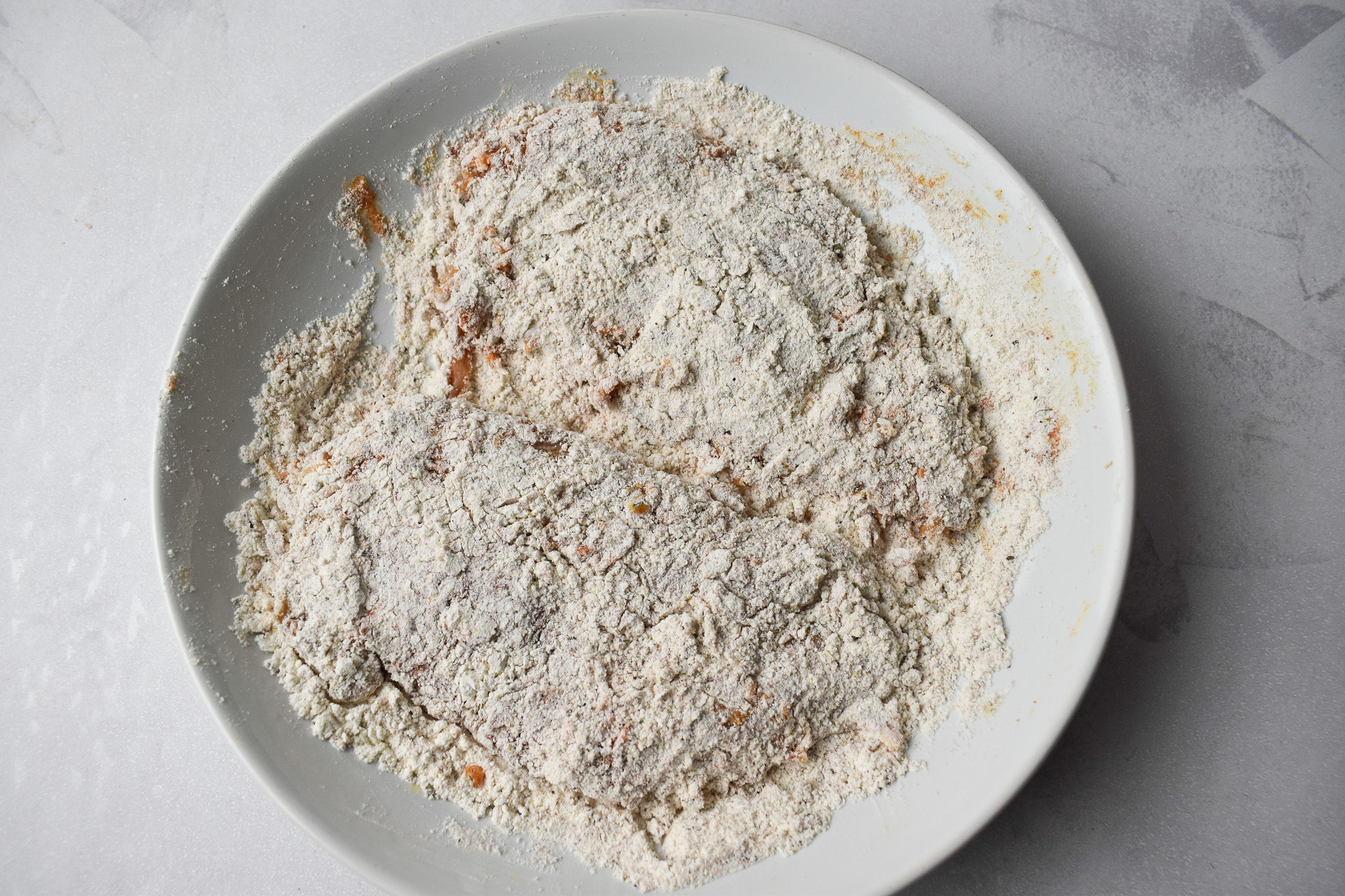 Raw chicken breast coated in seasoned flour.