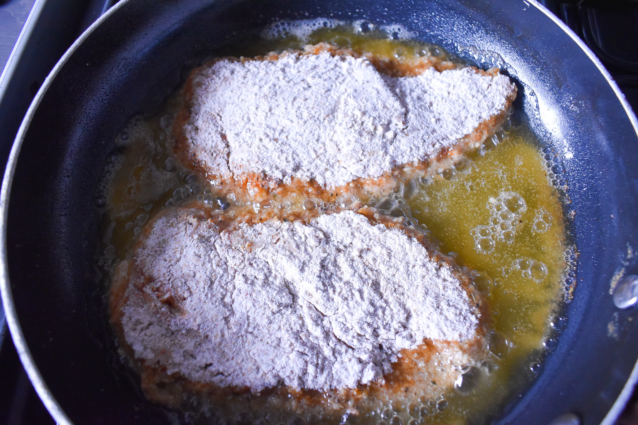 2 chicken breasts pieces being cooked in frying pan.