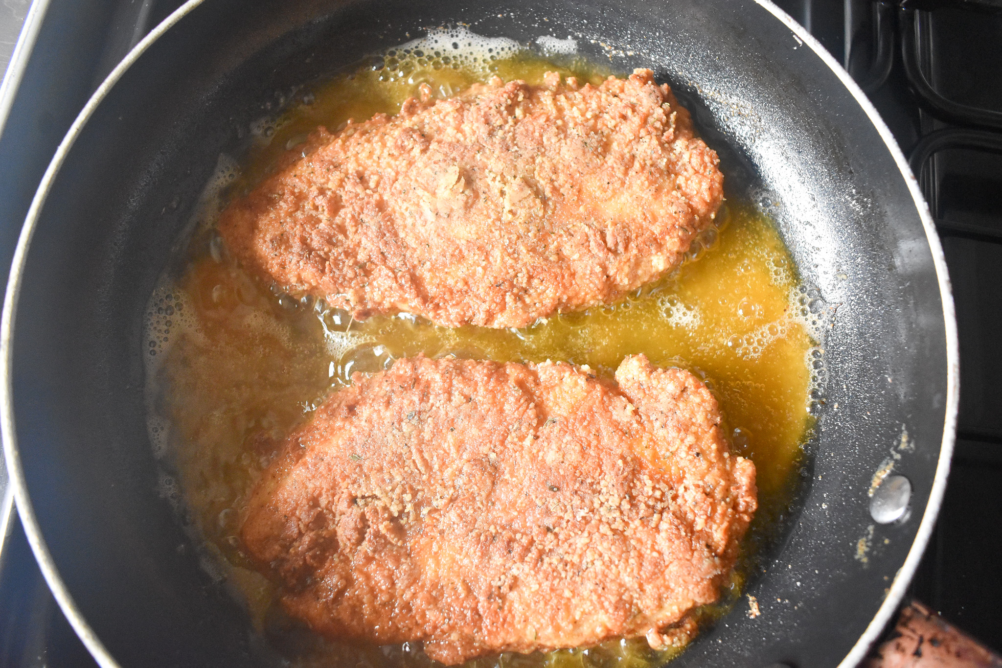 2 chicken breast pieces cooking in frying pan.
