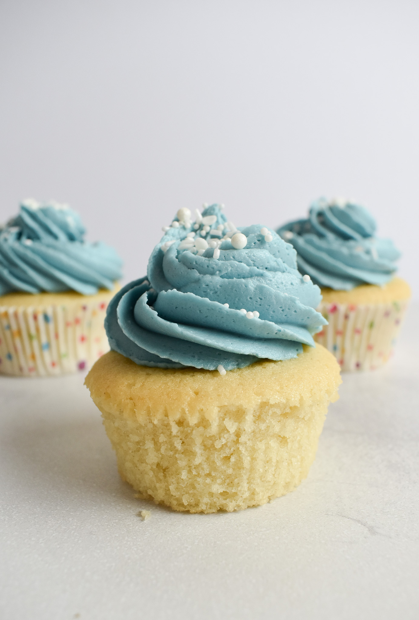 Vanilla cupcake removed from cupcake case with blue frosting.