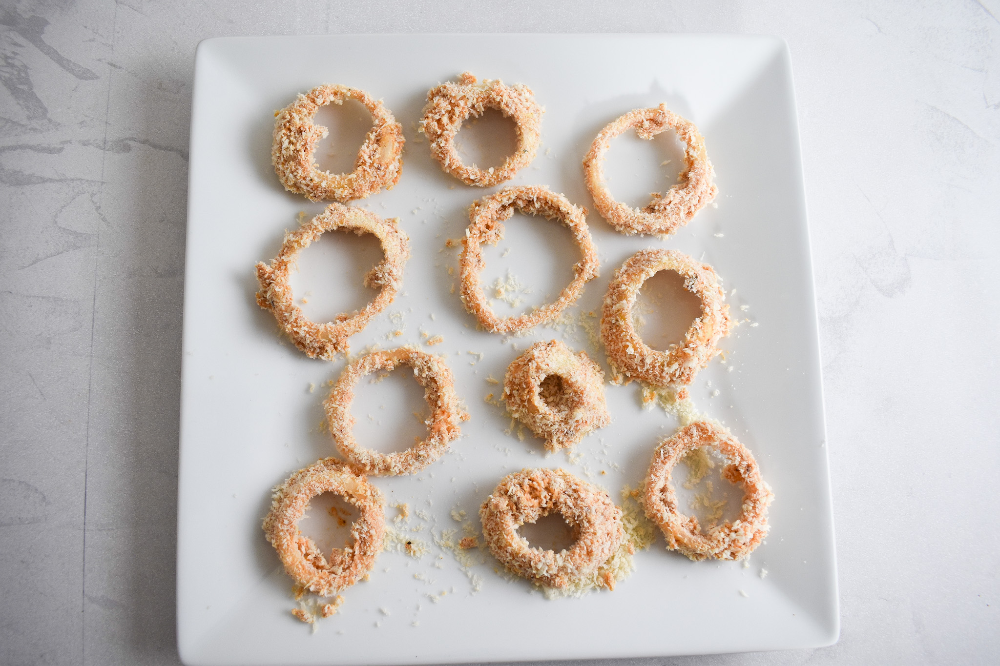 Breaded uncooked onion rings on plate.
